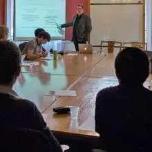 Students sit around a large wooden table as Harvey Brown delivers the seminar